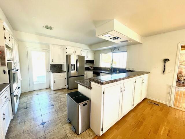 kitchen featuring dark stone countertops, kitchen peninsula, stainless steel refrigerator with ice dispenser, wall oven, and white cabinets