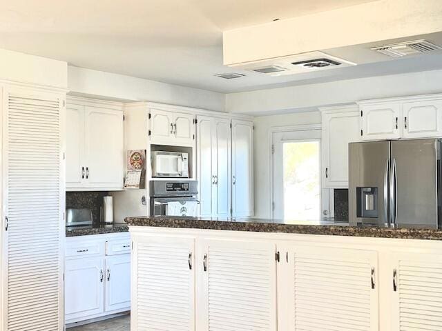 kitchen with decorative backsplash, white cabinetry, stainless steel appliances, and dark stone counters