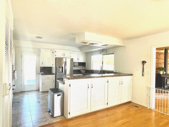 kitchen featuring backsplash, light hardwood / wood-style floors, kitchen peninsula, stainless steel refrigerator with ice dispenser, and white cabinetry