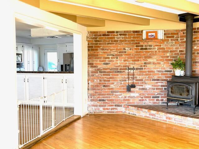 unfurnished living room with brick wall, a wood stove, and hardwood / wood-style flooring