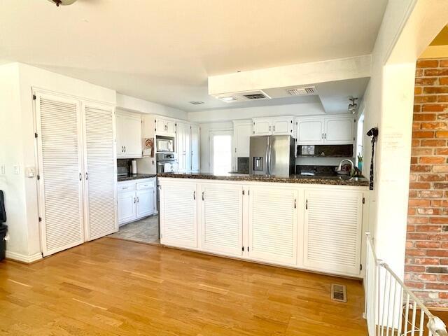 kitchen featuring white cabinets, kitchen peninsula, appliances with stainless steel finishes, and dark stone countertops