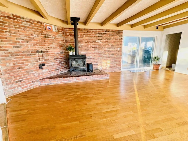 unfurnished living room with wood-type flooring, beamed ceiling, a wood stove, and a textured ceiling