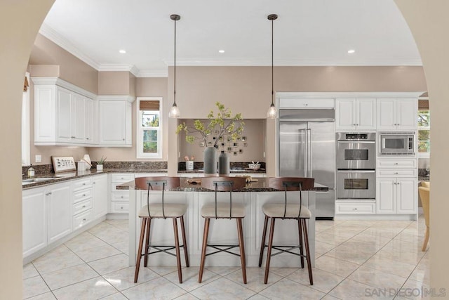 kitchen with built in appliances, a center island, dark stone countertops, and white cabinetry