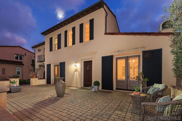 back house at dusk featuring french doors and a patio