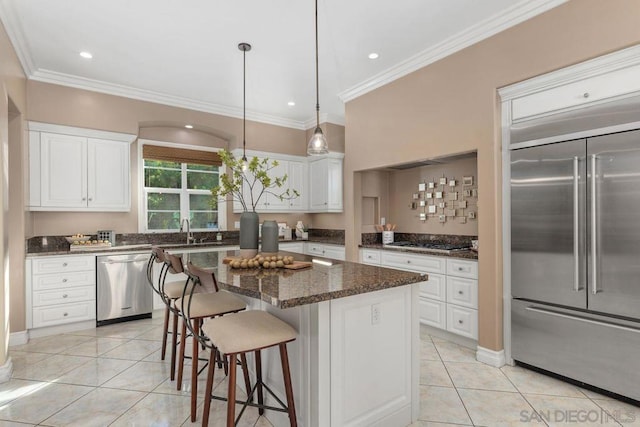 kitchen featuring a center island, dark stone counters, appliances with stainless steel finishes, light tile patterned flooring, and white cabinetry