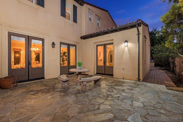 back house at dusk featuring french doors and a patio