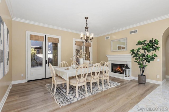 dining room with light wood-type flooring, ornamental molding, and an inviting chandelier