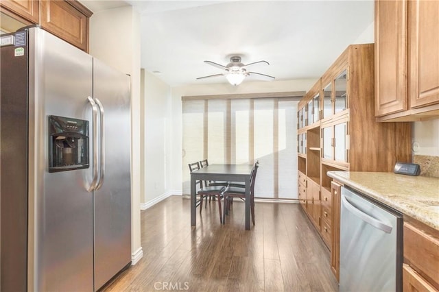 kitchen with appliances with stainless steel finishes, hardwood / wood-style flooring, light stone counters, and ceiling fan