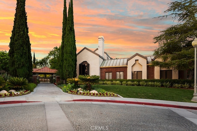 exterior space featuring stucco siding, a chimney, metal roof, a standing seam roof, and a front yard