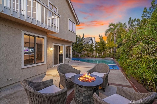 view of patio with a fire pit, a balcony, and a fenced in pool