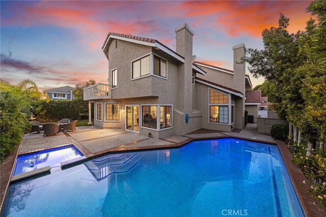 pool at dusk with an in ground hot tub and a patio