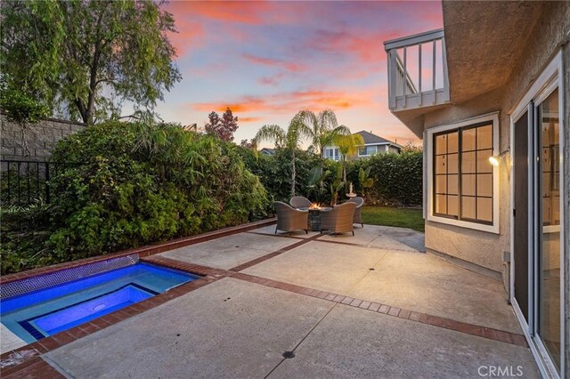 patio terrace at dusk featuring a balcony and an in ground hot tub