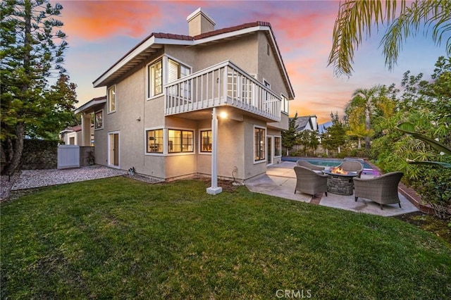 back house at dusk featuring a lawn, a patio area, and a balcony