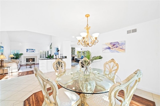 dining room with light tile patterned floors, lofted ceiling, visible vents, a glass covered fireplace, and a chandelier