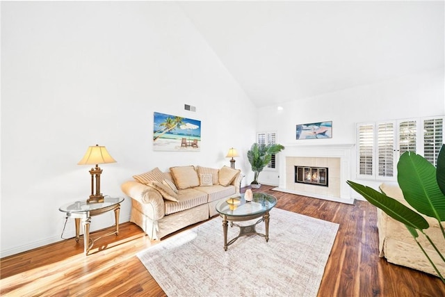 living area with high vaulted ceiling, visible vents, a tiled fireplace, and wood finished floors