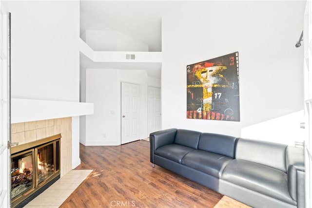 living area featuring high vaulted ceiling, visible vents, wood finished floors, and a tile fireplace