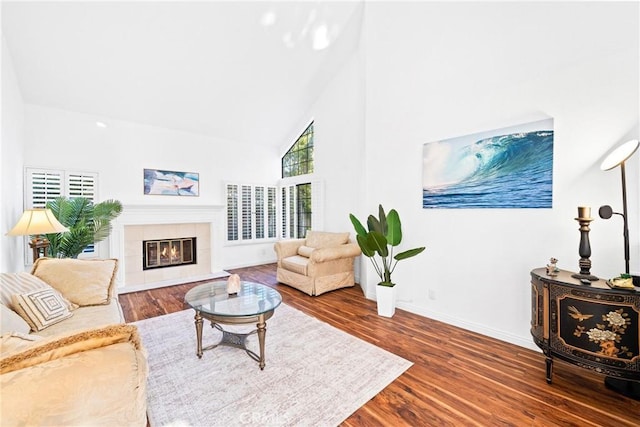 living room featuring high vaulted ceiling, a fireplace, wood finished floors, and baseboards