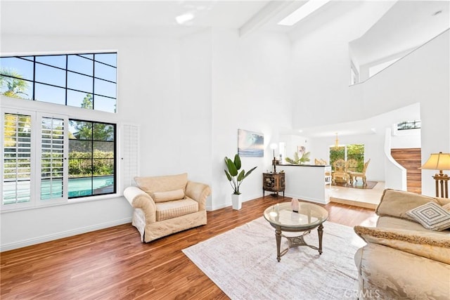 living room with a skylight, a high ceiling, baseboards, and wood finished floors