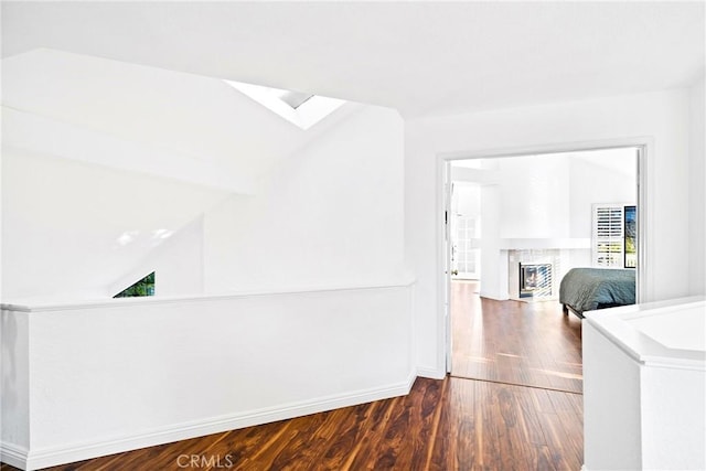 corridor with vaulted ceiling with skylight, baseboards, and wood finished floors