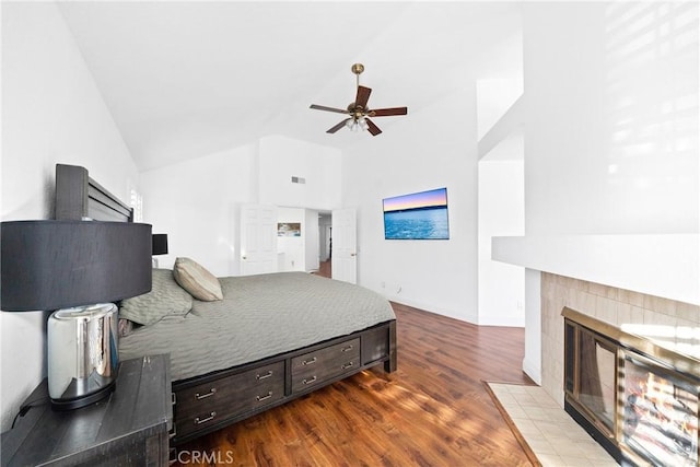 bedroom featuring lofted ceiling, wood finished floors, visible vents, baseboards, and a tiled fireplace