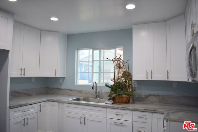 kitchen featuring white cabinetry, sink, and light stone counters