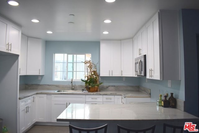 kitchen featuring white cabinets, a breakfast bar, kitchen peninsula, and sink