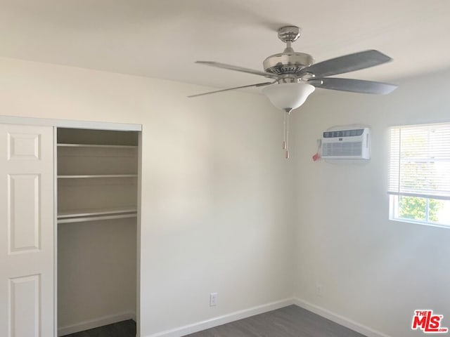 unfurnished bedroom with a closet, an AC wall unit, ceiling fan, and dark wood-type flooring