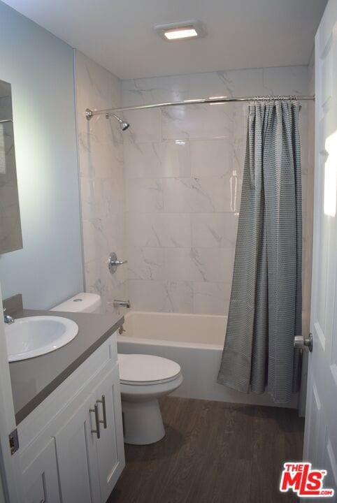 full bathroom featuring toilet, hardwood / wood-style floors, vanity, and shower / tub combo with curtain