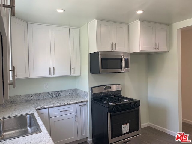 kitchen featuring light stone countertops, stainless steel appliances, dark wood-type flooring, sink, and white cabinetry