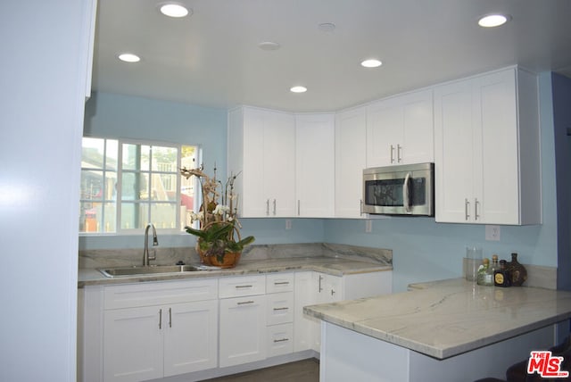 kitchen with white cabinets, light stone counters, kitchen peninsula, and sink