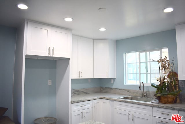 kitchen with light stone countertops, sink, and white cabinets