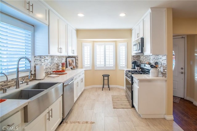 kitchen featuring decorative backsplash, appliances with stainless steel finishes, light stone counters, sink, and white cabinetry