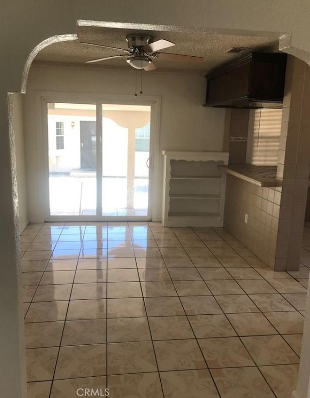 tiled empty room with ceiling fan and a textured ceiling