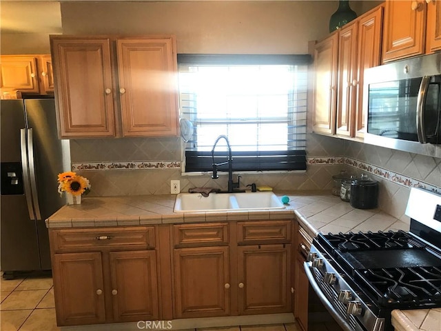 kitchen with tile counters, sink, stainless steel appliances, tasteful backsplash, and light tile patterned floors