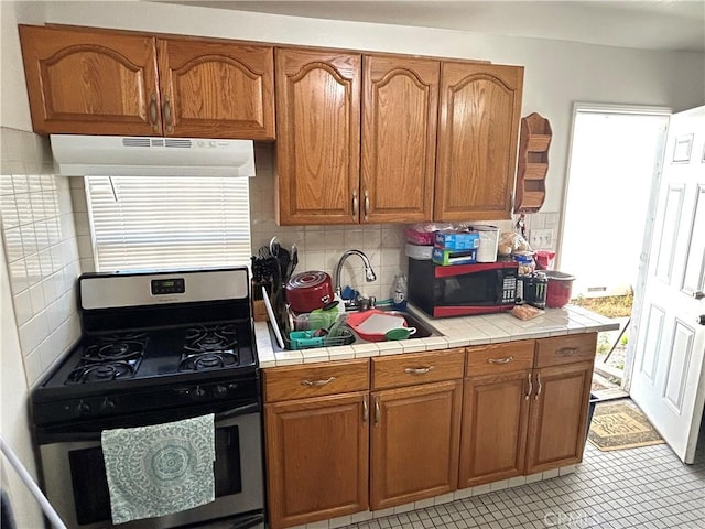 kitchen featuring stainless steel gas range oven, sink, decorative backsplash, light tile patterned floors, and tile counters