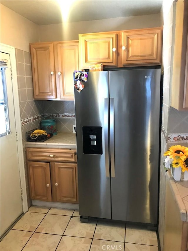 kitchen featuring backsplash, tile countertops, light tile patterned flooring, and stainless steel refrigerator with ice dispenser