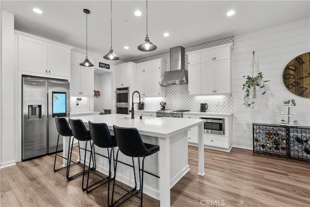 kitchen featuring white cabinets, appliances with stainless steel finishes, light hardwood / wood-style floors, and wall chimney exhaust hood