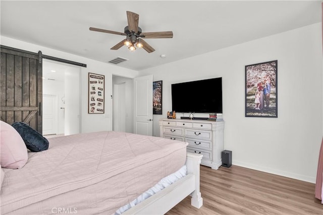 bedroom with a barn door, ceiling fan, and light hardwood / wood-style floors