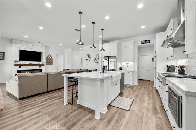 kitchen with light hardwood / wood-style flooring, a fireplace, white cabinetry, hanging light fixtures, and an island with sink