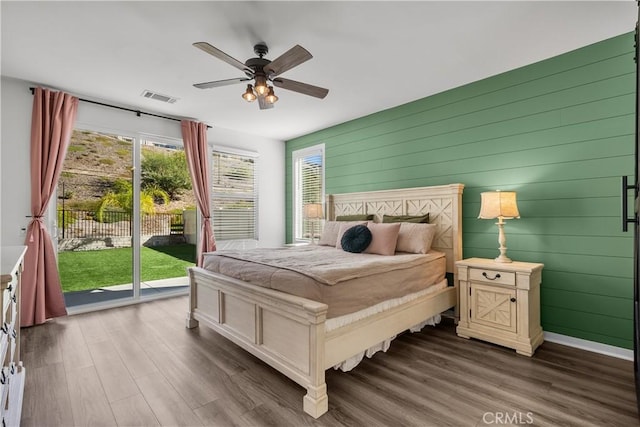 bedroom with access to exterior, dark hardwood / wood-style floors, ceiling fan, and wood walls