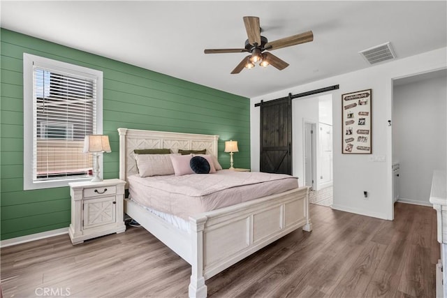 bedroom with a barn door, hardwood / wood-style flooring, ceiling fan, and wood walls