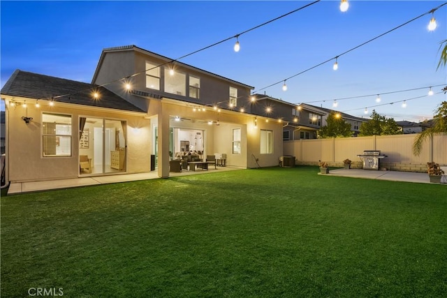 back house at dusk featuring ceiling fan, a patio area, and a lawn