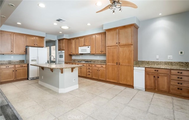 kitchen with a breakfast bar, white appliances, sink, ceiling fan, and light stone countertops