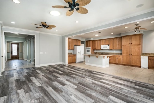 38548 Falkirk Dr, Murrieta, CA 92563 - kitchen with white appliances, a ceiling fan, ornamental molding, a kitchen bar, and brown cabinetry