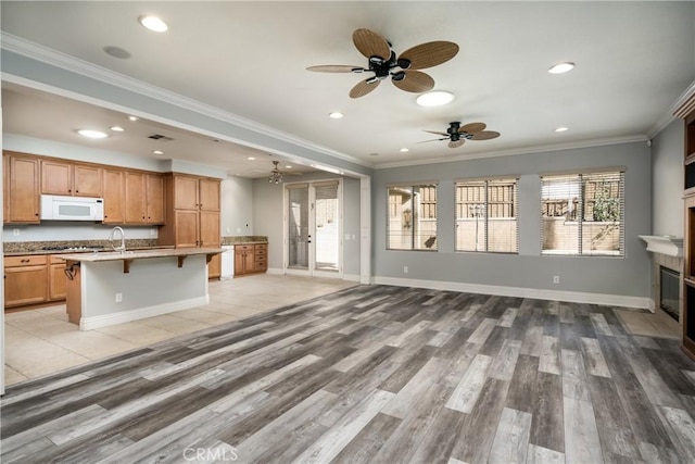 kitchen featuring crown molding, an island with sink, light hardwood / wood-style floors, white appliances, and a kitchen bar