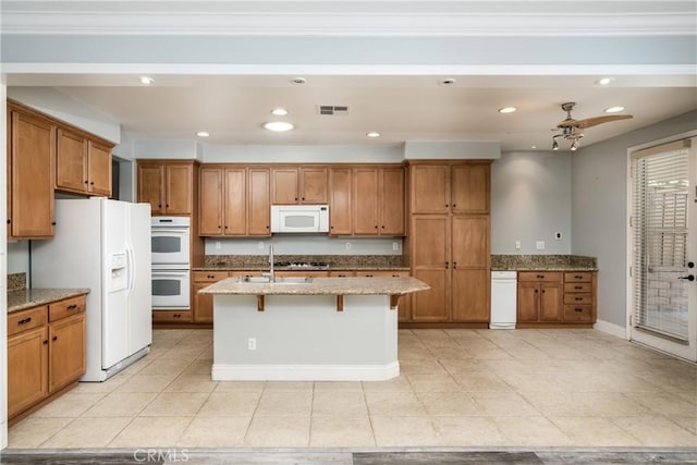 kitchen with ceiling fan, light stone countertops, white appliances, a kitchen island with sink, and a breakfast bar