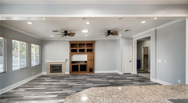 unfurnished living room with dark hardwood / wood-style floors, ceiling fan, crown molding, and a tiled fireplace