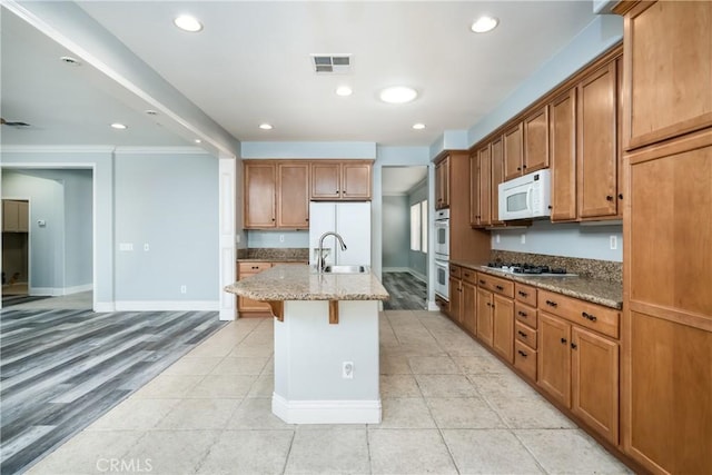 kitchen featuring light stone countertops, a kitchen bar, white appliances, light hardwood / wood-style floors, and an island with sink