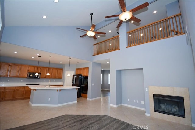 kitchen with a fireplace, a center island with sink, high vaulted ceiling, and sink