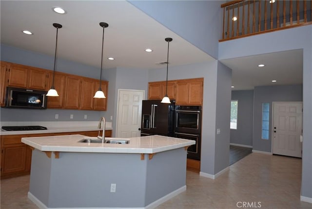 kitchen featuring tile countertops, a kitchen island with sink, black appliances, sink, and light tile patterned flooring